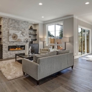 Living room interior in gray and brown colors features gray sofa atop dark hardwood floors facing stone fireplace with built-in shelves