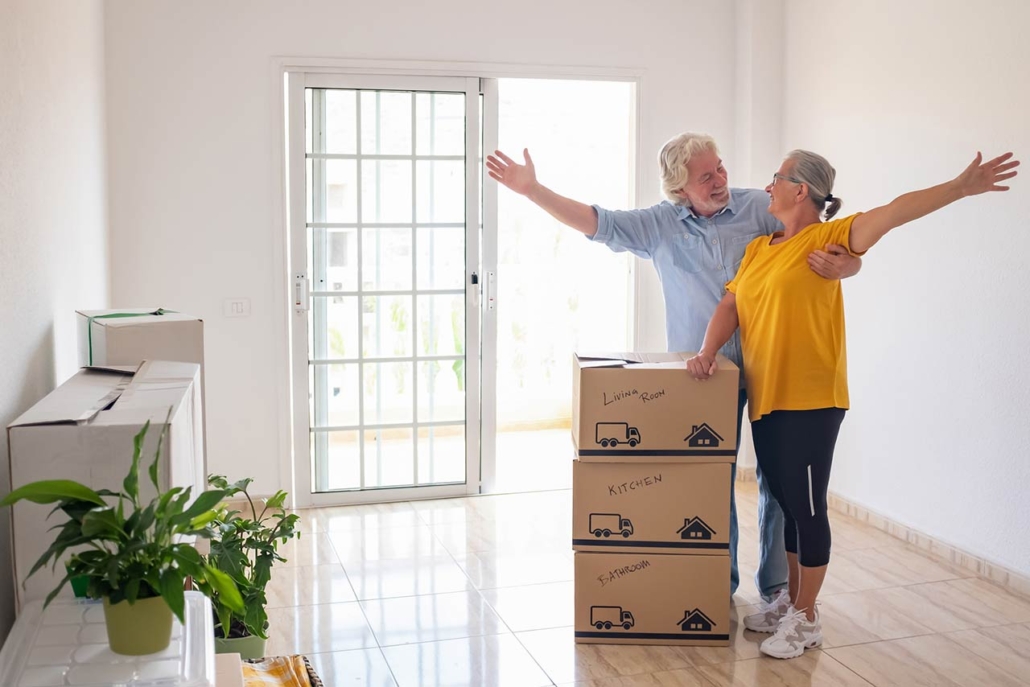 Smiling caucasian senior couple white haired open arms looking at each other's eyes during relocation, excited for a new beginning