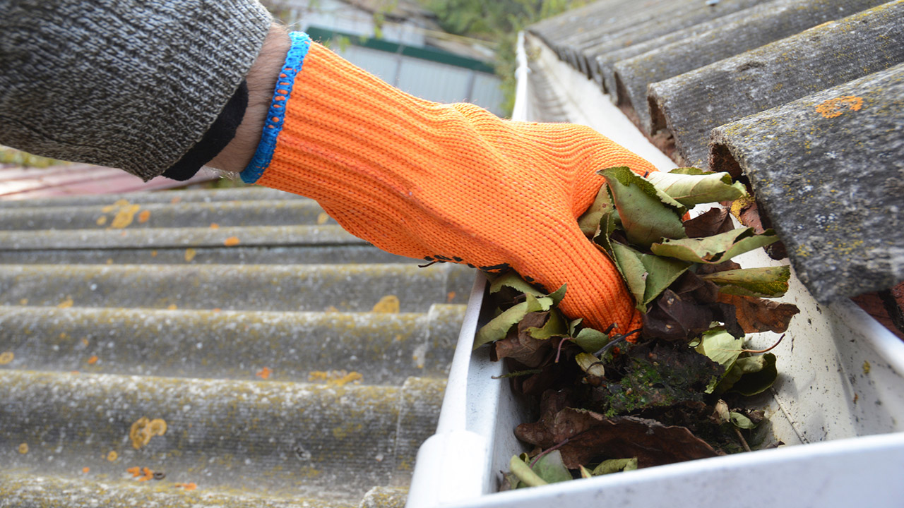 Roofer cleaning a rain gutter with an orange glove on