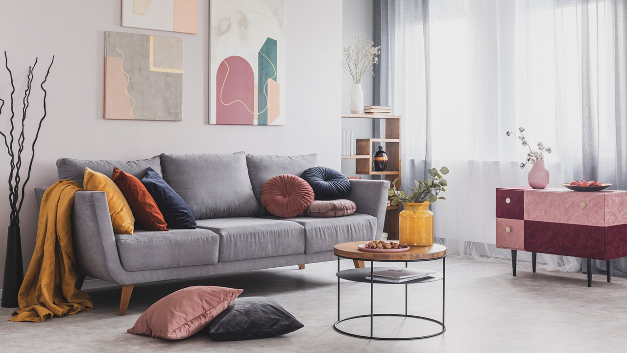 Real photo of abstract paintings hanging on white wall above a gray sofa in a living room interior with big windows