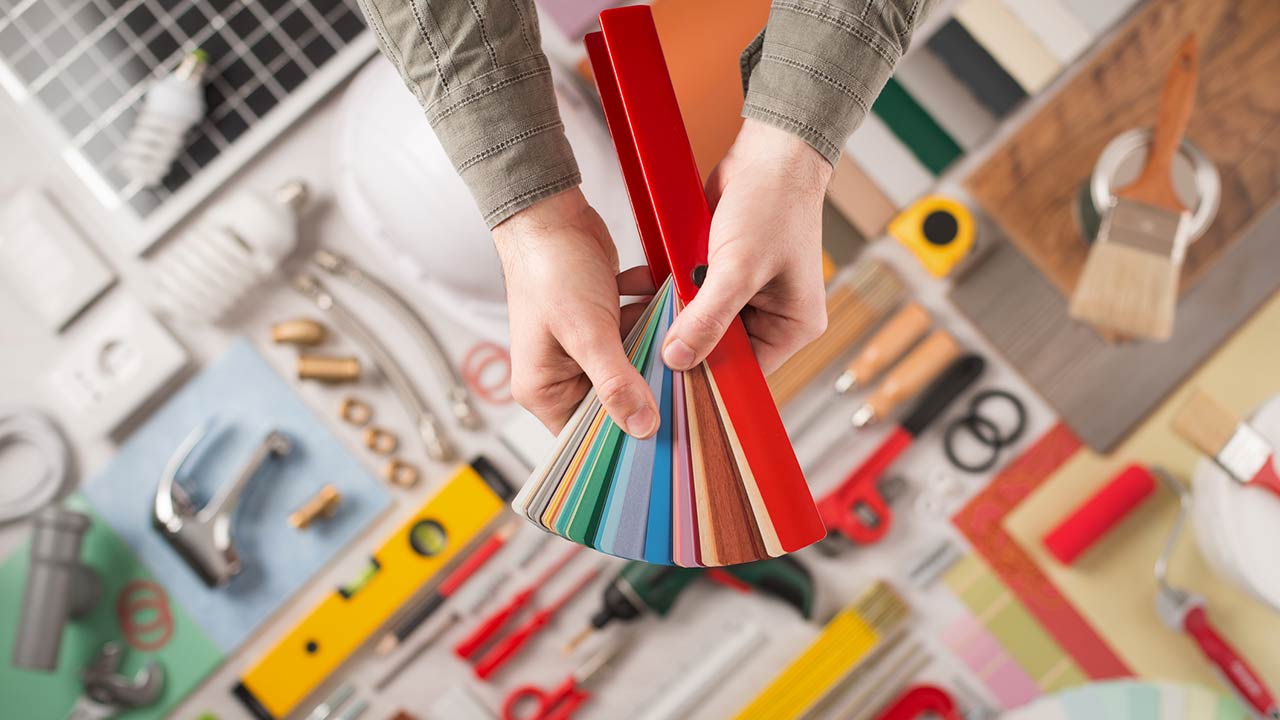 Male hands holding swatches and choosing the right color, work tools on background top view