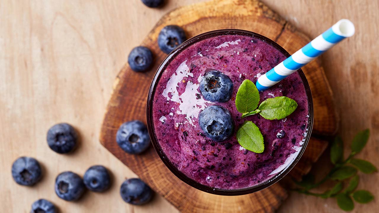 Glass of blueberry smoothie on wooden background from top view