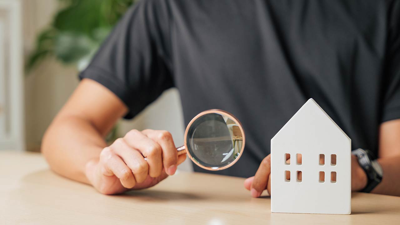 Hand with a magnifying glass examines a block house for real estate purposes