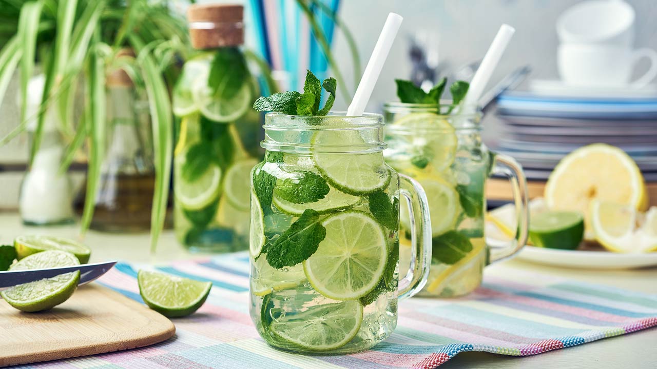 Two glasses and a bottle of homemade lemon, lime, and mint lemonade sit on the wooden dining table