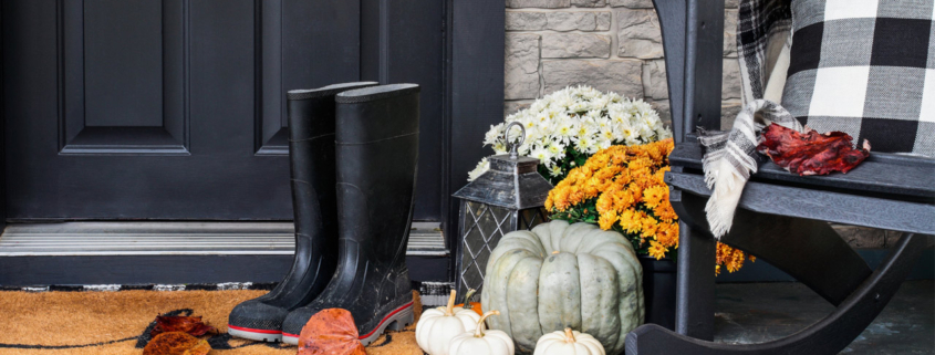 Traditional style front porch decorated for autumn with rain boots, heirloom gourds, white pumpkins, mums and rocking chair
