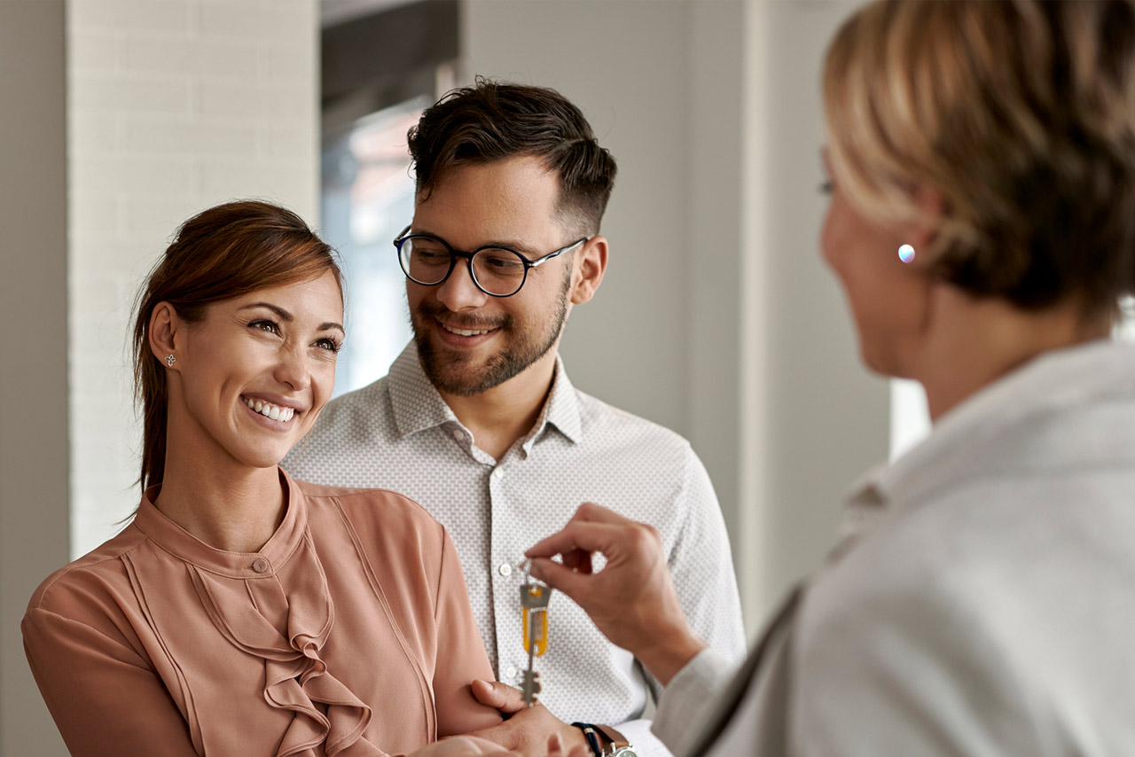 Happy couple buying new home and receiving house keys form real estate agent