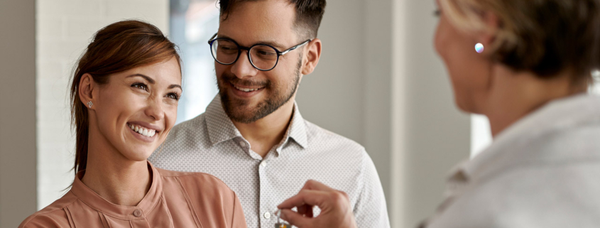 Happy couple buying new home and receiving house keys form real estate agent